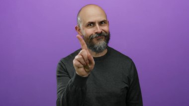 Mor arka planda sakallı kel bir adam. El işaretleri ve dövmesi ile ihtiyatlı olduğunu söylüyor..