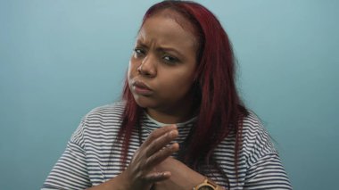 Kadın stüdyoda yumruğunu sıkar ve kaşlarını çatar açık mavi arka planla; öfke gerilimi.