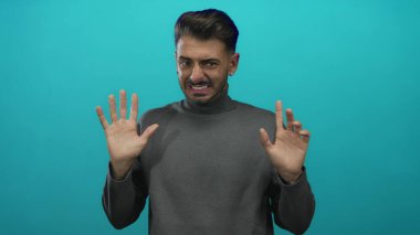 Stüdyoda dur demek için turkuaz arka planda gri balıkçı yaka giyen bir adam avuçlarını dışarı kaldırır..
