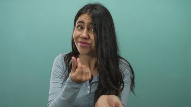 Genç İspanyol kadın, yeşil duvara karşı stüdyoda para için el kaldırıyor, işaret işareti yapıyor; acil savunma.