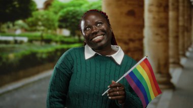 Şehir caddesinde elinde gökkuşağı bayrağı tutan kadın dışarıda şehir merkezine karşı neşeli bir ifadeyle LGBT gururunu kutluyor..