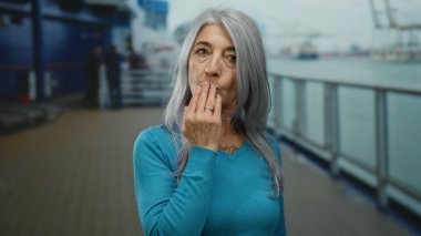 Gri saçlı son sınıf öğrencisi kadın, bir deniz gezisinde kameraya bir öpücük yolluyor. Gülümsüyor ve teknede rahatlatıcı bir açık hava anının tadını çıkarıyor..