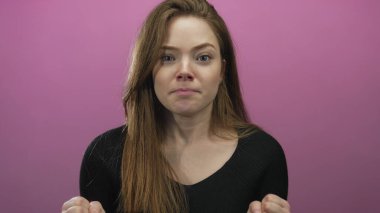 Kadın yumruklarını sıkıyor ve elini kaldırıyor. Stüdyoda pembe arka planda geniş bir sırıtış ve neşeli bir ifadeyle..