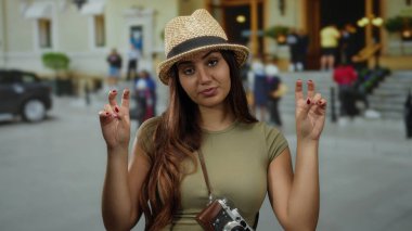 Kameralı ve şapkalı İspanyol kadın sokak ortamında barış işaretleri gösteriyor. Sıradan bir turist havası yayıyor..