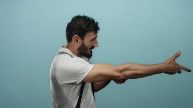 Sakallı İspanyol bir adam. Mavi arka planda ip çekiyormuş gibi yapıyor. Espri anlayışı ve kas gerilimi gösteriyor..