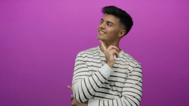 Genç, ispanyol, elleri çenesinde çizgili tişört giyen soyutlanmış, pembe arka planda tefekkür ve karar verme mekanizmasını gösteren bir adam..