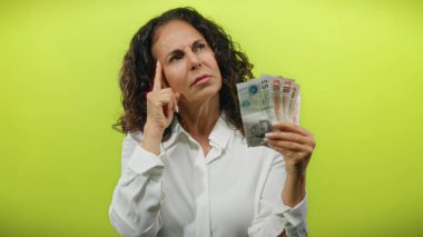 Sarı arka planda İngiliz banknotlarını tutan orta yaşlı bir kadın. Düşüncelerini ve memnuniyetini kapalı gözlerle ifade ediyor ve parmağını kaldırıyor..