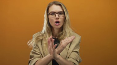 Gözlüklü sarışın kadın, turuncu arka planda çapraz kollarla reddedildiğini ifade ediyor..