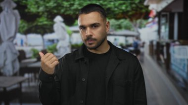 Adam teras inşaatında, bulanık masalara ve şemsiyelere tepeden bakan çıplak baş parmağını gösteriyor; iyimserlik.