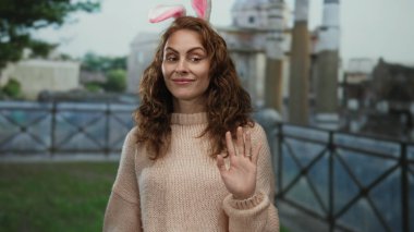 Tavşan kulaklı genç bir kadın tarihi Roma harabelerinin yanında gülümsüyor, süveter giyiyor, arka planda Roma mimarisi, eğlence ve tarihi harmanlıyor..