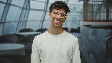 İnsan, modern restoranın içinde gözlük ve beyaz kazak giyerken dudaklarına dokunur ve sessiz bir jest yapar..