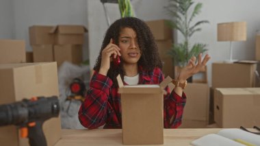 Kadın, binadaki düzenli masada kırmızı akıllı telefonu kulağına tutan küçük bir karton kutuyu açıyor..