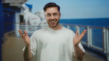 Gemi güvertesinde sırıtan sakallı genç bir adam açık havada güneşli bir günde deniz zeminine gülümsüyor..