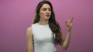 Uzun saçlı ve elini kaldırmış, pembe stüdyoda omuz silken beyaz atlet giyen İspanyol bir kadın..