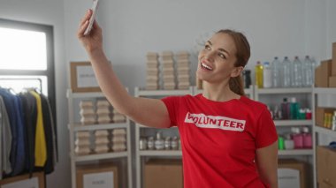 Kırmızı tişörtlü genç bir kadın, bağış merkezi binasında selfie çektirmek için akıllı telefonu kol mesafesinde tutuyor.. 