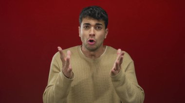 Erkekler, arka plan kırmızısı ve endişeli ifade ile genç İspanyol erkeğin stüdyo portresinde el kaldırır..