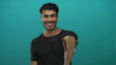 Tebessüm eden adam Teal stüdyosunda el sıkışmak için sıcak bir şekilde elini uzatır; hoş geldin bağlantısı güven dostluğu.