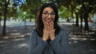 Kadın, altın öğleden sonra ışığı altında güneşli yeşil ağaçların altında elleri ile ağzını kapatıyor. Sürpriz..