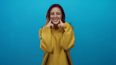 Sarı bir kazak içinde neşeli bir şekilde poz veren bir kadın canlı mavi bir arkaplan karşısında neşeli ve çekici bir anı yakalıyor..