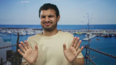 Yükselmiş avuç içleri olan bir adam rıhtımlı tekneleri olan güneşli bir caddede reddedilme jesti ile ileriye itildi..