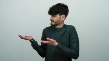 Siyah saçlı ve sakallı genç adam süveter giyiyor, izole edilmiş beyaz bir arka plan üzerinde hareketler yapıyor..