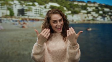 Hareketli bir sahil sahilinde gülümseyen bir kadın açık mavi bir gökyüzünün altında insanlarla dolu rahat bir süveter ve tepeler giyiyor..