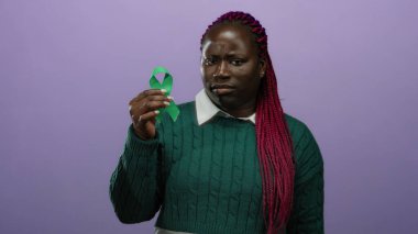 Yeşil kurdele tutan Afrikalı Amerikalı kadın, izole edilmiş mor bir arka plan duvarına karşı duruyor, farkındalık ve çeşitlilik gösteriyor..