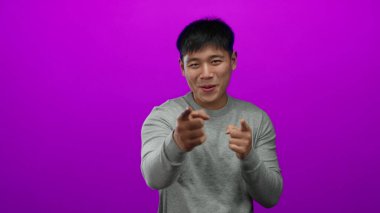 Genç adam parlak pembe bir arkaplanı işaret ediyor ve gülümsüyor, günlük gri bir gömlek giyiyor, stüdyo ortamında izole edilmiş, pozitiflik ve nişan iletiyor..