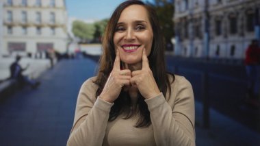 Canlı bir şehir caddesinde gülümseyen bir kadın neşeli bir ifade ve mutluluk sergiliyor, güneşli bir arka planda neşeli tavırlarıyla gün ışığında harmanlanıyor..