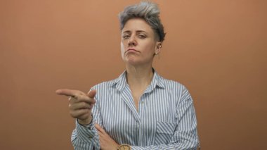 Çapraz kollu ve turuncu stüdyoda sert ifadeli, çizgili gömlek giyen bir kadın. Kararlılık..