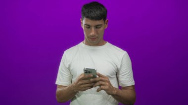 İki eliyle akıllı telefonu tutan adam mor stüdyodaki dokunmatik ekranda konsantre bakışla mesajlar atıyor..