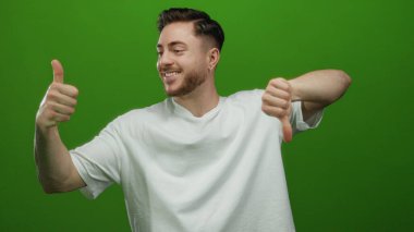 Sakallı genç adamın jestleri, canlı yeşil arkaplan karşısında dikilip duruyor. Beyaz gömlek giyiyor ve duygularında pozitif negatif bir kontrastlık gösteriyor..