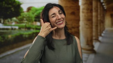 İspanyol orta yaşlı kadın sütunları inşa ederken eli kulağında çağrı jesti yapıyor; iletişim bağlantısı sevinç sıcaklığı.