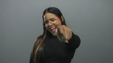 Gri arka planda neşeli bir tebessümle canlı ve anlamlı bir poz yakalayan bir kadın..