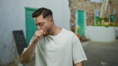 Şehir caddesinde beyaz bir gömlekle duran genç bir adam göğsünü tutan düşünceli bir yüz ifadesiyle, bulanık şehir manzarasıyla çevrili..