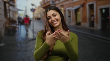 Genç İspanyol kadın açık bir caddede davetkar bir şekilde gülümsüyor açık bir şehir ortamında neşeli bir ifade sergiliyor neşeli bir şehir havası yakalıyor..