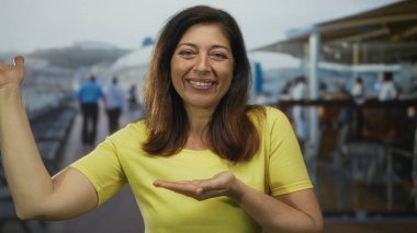 Karşılama jestinde avuç içi sunan ve yolcu güvertesinde gülümseyen kadın, neşeli bir selamlama..