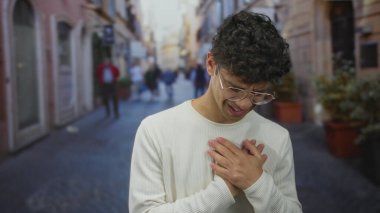 Kalabalık şehir caddesinde yuvarlak gözlüklü ve beyaz kazaklı bir adam el ele tutuşuyor..