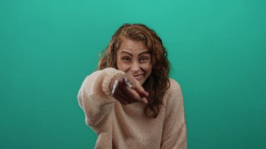 Yeşil bir arka plan önünde neşeli bir şekilde gülen, rahat bir kazak giyen, mutluluk ve kaygısız duyguları ifade eden, samimi bir kahkaha anında yakalanan bir kadın..