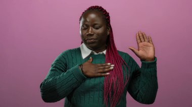 Göğsünde el olan Afrikalı Amerikalı kadın, izole edilmiş pembe arka plana karşı yemin ediyor. Samimiyet ve bağlılık ifade ediyor..
