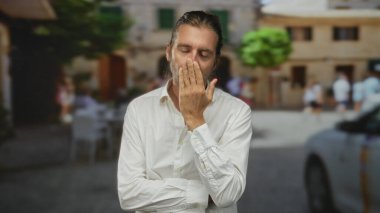 Uzun sarı saçlı, beyaz gömlekli bir adam güneş ışığında sessiz kalmak için el ele tutuşuyor..