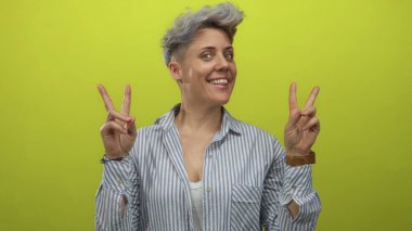 Kısa saçlı, gülümseyen beyaz kadın çizgili gömlek ve bileziklerle stüdyoda barış işareti gösteriyordu. Mutluluk..