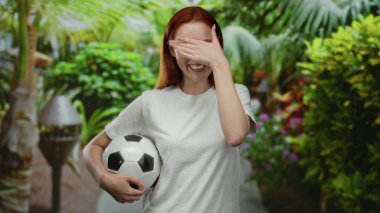 Yeşil bir park ortamında elinde futbol topuyla gülümseyen bir kadın, gençliğini ve mutluluğunu canlı bir arka planda sergiliyor..
