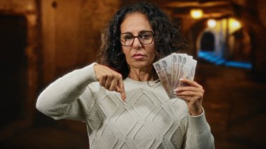 Dışarıda elinde Rus rublesi olan bir kadın geceleri şehir sokağında ciddi bir ifadeyle gözlük ve süveter takıyor..