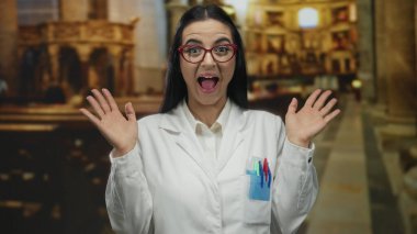 Beyaz önlüklü, kırmızı gözlüklü bir kadın kilise ortamında bilim ve maneviyatın bir karışımını gösteren ifadeler kullanıyor..