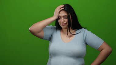 Artı mavi kazaklı kadın, izole edilmiş yeşil arka plana karşı hayal kırıklığı gösteriyor.