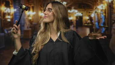 Siyah cüppeli kadın yargıç, sağ elini kaldırmış tahta tokmak tutuyor ve mermer mahkeme salonunda sol avuç içindeki pirinç dengeleri dengeliyor; adalet otoritesini dengeliyor.