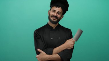 Sakallı İspanyol erkek aşçı canlı yeşil bir arka planda siyah bir üniformayla satırı kavrıyor..