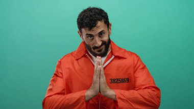 Turuncu hapishane tulumlu İspanyol sakallı adam yeşil bir geçmişe karşı dua ediyor. Hapis içinde umut ve iç gözlem taşıyor..