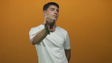 Genç İspanyol adam doğrudan kameraya bakıyor ve stüdyoda turuncu arka planda boğaz kesme hareketi yapıyor..